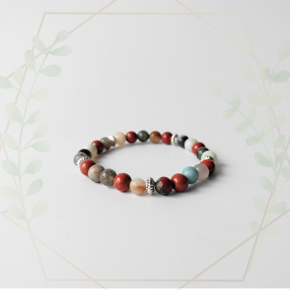 A multicolored bracelet with a mix of bloodstone, red jasper, and amazonite gemstones, displayed against a white background with a decorative plant in the background.