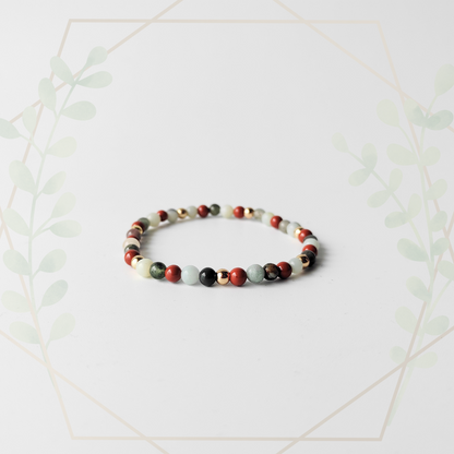 A multicolored bracelet with a mix of red, black, and green gemstones, displayed against a white background with a decorative leafy border.