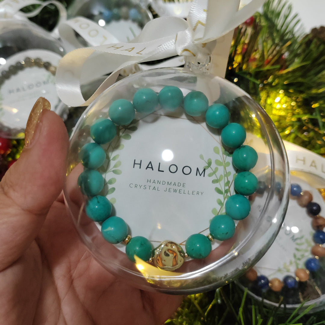 Turquoise beaded bracelet in a clear plastic case with 'HALOOM' branding, held against a festive background.