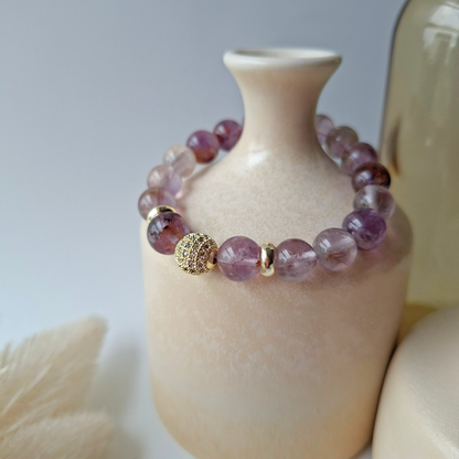 Purple phantom quartz bracelet with gold accents on a beige vase against a neutral background